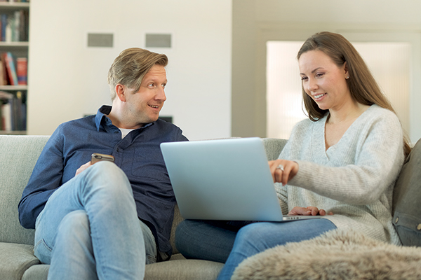 Smilende mann og kvinnesom sitter i sofaen og ser på en bærbar datamaskin